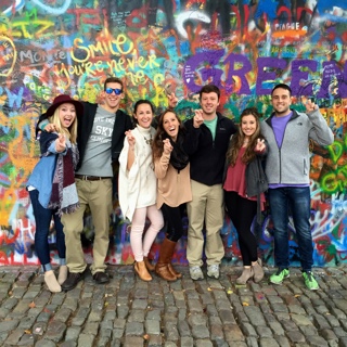 Seven TCU students studying abroad stand in front of a brightly spray-painted graffitti wall on a cobblestone street in Prague.