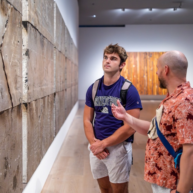 TCU student look at art on wall while professor gestures to the piece