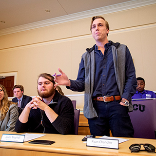 A male student stands to speak at a TCU student government meeting in the chambers of the student union.