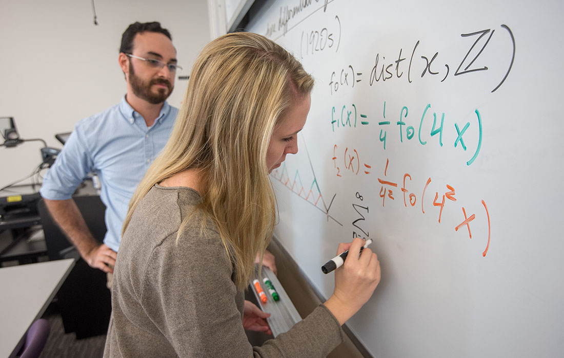 Math class with student solving a problem on a whiteboard.