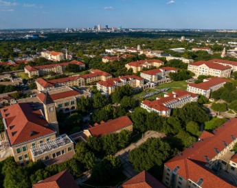 Aerial view of TCU's west campus rooftops with Fort Worth cityscape in background.